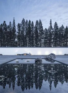 A serene minimalist landscape featuring concrete pavement, water reflections, and stone accents.