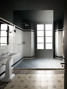 An industrial-style bathroom with white tiles, featuring a shower area, a pedestal sink, and a glass door.