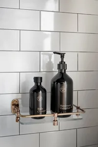 A minimalist bathroom shelf made of metal and glass, featuring black bottles of body cleanser and handwash.