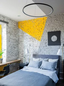 A minimalist bedroom with a brick wall, featuring a bed with striped bedding, a hanging circular light fixture, and a desk wi