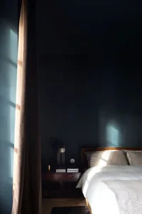 A minimalist bedroom with a white bed, wooden floor, and dark blue walls.