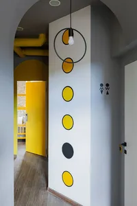 A minimalist grey wall features circular yellow accents and a hanging black light fixture.