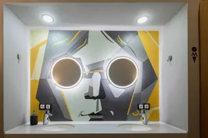 A modern art mural featuring abstract shapes and large circular lights behind two sinks in a bathroom setting.