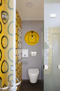 A contemporary bathroom with yellow patterned tiles, a white toilet, and a circular light fixture.
