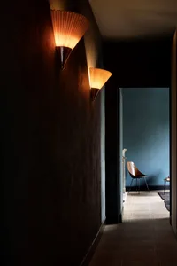 A modern corridor featuring concrete walls with two sconces illuminating the space, leading to a room with a blue wall and a 
