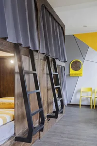 A modern hostel bedroom with bunk beds featuring grey curtains and yellow accents, with black ladders leading to the beds.