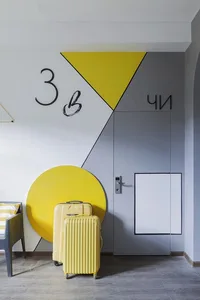 Modern hotel suite entry with a white and yellow triangle wall design and yellow luggage.