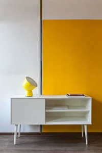 A modern living room with a white cabinet, yellow floor lamp, and books, featuring bold yellow accent walls.