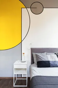 A modern minimalist bedroom featuring a grey upholstered bed, a white metal nightstand with a small glass and a cork bottle, 