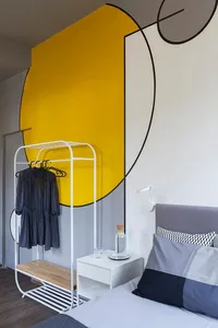 A modern minimalist bedroom with a geometric wall mural, grey bedding, and a white hanging rack.