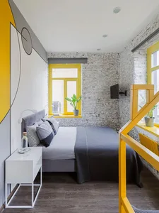 A modern bedroom featuring a concrete wall and wooden floor with a yellow window frame and a gray bed.