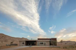 Modern residential exterior of a house in a desert landscape with a clear blue sky above.