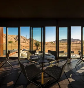 Modern restaurant interior with glass windows, metal dining furniture, and a view of the desert.