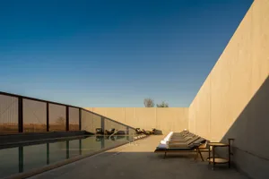 A modern swimming pool area with concrete walls and a clear blue sky.