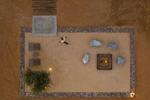 A desert outdoor living space with a fire pit, rocks, gravel, and a person walking nearby.