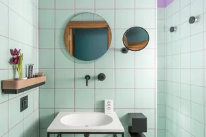 Bathroom with green and white tiled walls featuring a sink, mirror, and purple accents.
