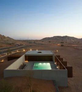 Modern concrete structure with a pool and lounge area in a desert landscape.