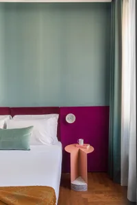 A modern minimalist bedroom featuring a white bed with a green throw pillow and a unique, geometric-shaped wooden side table.