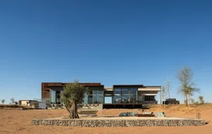 A modern residential building with large glass windows, surrounded by desert landscape.