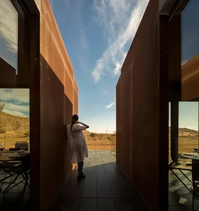 A modern rustic vacation home with a metal clad exterior set against a desert backdrop.