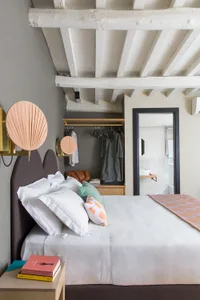 A minimalist bedroom with wooden beams on the ceiling, white bed linens, and pastel-colored pillows.