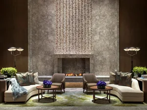 Modern hotel lobby featuring a fireplace, chairs, and tables with flowers.
