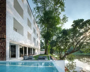 Modern hotel resort building with concrete exterior and outdoor seating area by a tranquil river.