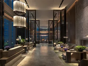 Modern lobby featuring metal light fixtures, wooden benches, glass panels, and stone flooring.