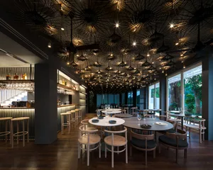 A modern restaurant interior with paper umbrellas hanging from the ceiling, wooden furniture, and a bar area with liquor bott