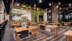 A modern, minimalist restaurant interior with wooden tables, concrete accents, and glass walls.