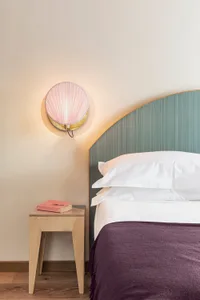 A modern bedroom featuring a bed with a curved headboard, white linens, and a bedside table with a pink lamp and a pink book.