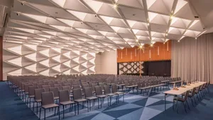 A spacious conference room with modern design elements, including geometric patterns on the ceiling and walls, and a stage ar