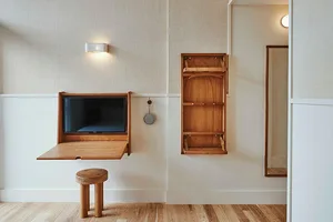 A minimalist modern residential space with a drop-down wooden table mounted on the wall, providing a multifunctional area for
