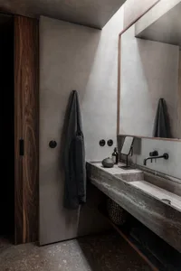 Minimalist bathroom featuring concrete walls, a black faucet, and a wooden towel rack.
