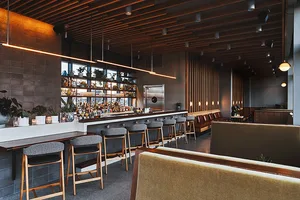 A modern restaurant bar interior featuring wooden walls, leather seating, and concrete flooring.