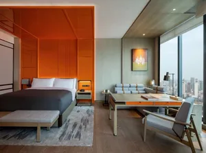 Modern bedroom with orange accent wall, wooden floor, and a view of the city.