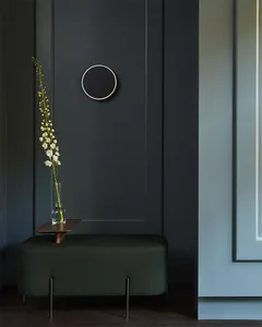 A modern entryway with a dark wooden bench and a vase of flowers placed on a small wooden table in front of a dark-paneled wa
