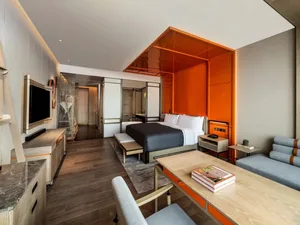 Spacious hotel room with modern design, featuring a wooden floor, metal accents, and glass partitions.