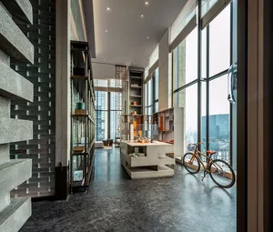 Modern, minimalist living space with concrete walls and floor, featuring a bicycle in the foreground and large windows offeri