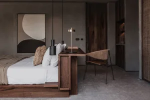 A modern minimalist bedroom featuring a bed with a wooden headboard, white bedding, and a wooden desk with a lamp.