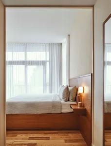 A modern minimalist bedroom featuring a wood-finished platform bed with striped bedding and a floating nightstand.
