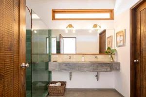 A modern minimalist bathroom with concrete walls and floors, a double sink vanity, and a walk-in shower enclosed by glass.