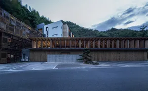 Modern residential building with wooden and concrete facade, set against a natural landscape with mountains in the background