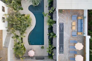 A modern vacation home with a swimming pool, wooden deck, and palm trees.
