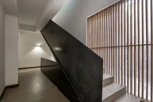 A minimalist black steel staircase with a wooden slatted wall in the background.