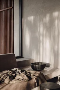 A minimalist living room featuring modern furniture on a concrete floor, with natural light streaming through a large window.