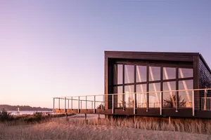 A modern, minimalist residential building with large glass windows and wooden exterior.