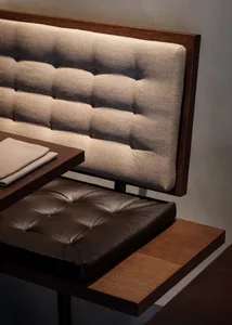 A modern bench seat with a tufted fabric backrest and a brown leather cushion on a wooden platform.
