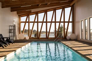 Modern industrial swimming pool with glass walls and wooden beams