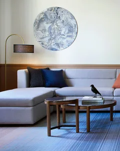 Modern living room featuring a sectional sofa with blue and gray upholstery, a glass coffee table, and a marble light fixture